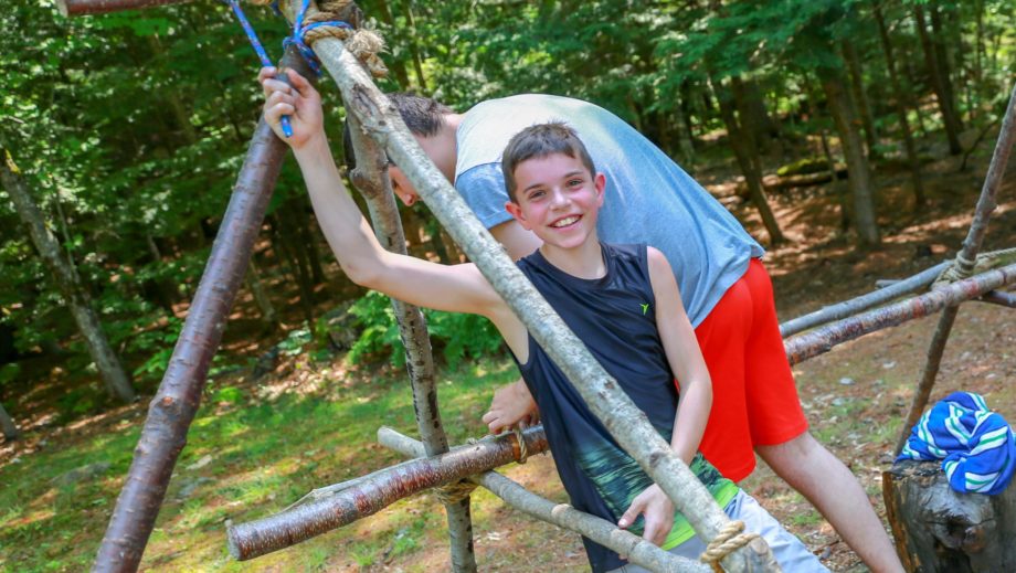 boy by wooden structure he built for outdoor living skills